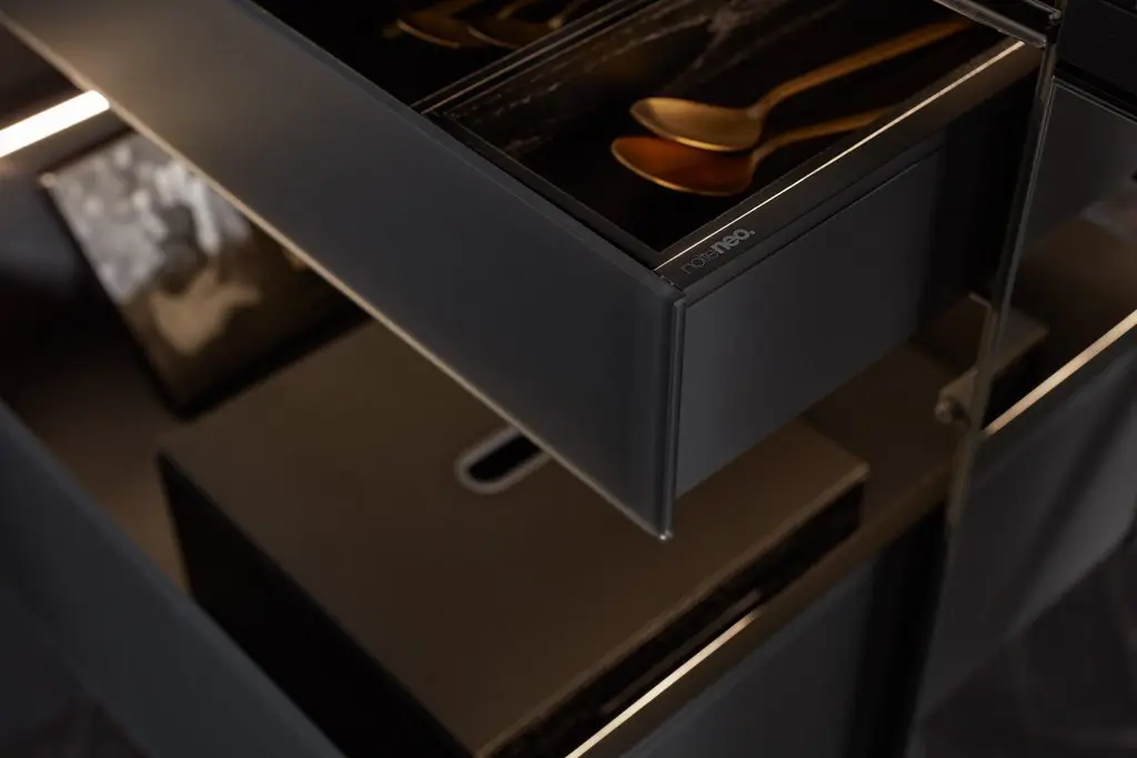 Detalj iz NolteNeo kuhinje sa fiokom u tamnoj mat boji, LED osvetljenjem i elegantno organizovanim zlatnim priborom, prikaz savremenog dizajna i vrhunske izrade unutrašnjih elemenata